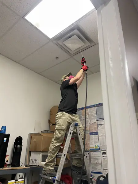 Technician working on a ceiling supply vent during commercial duct cleaning